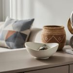 Contemporary living room console styled with a ceramic bowl and keys, a geometric pillow, a woven basket, and an abstract metal sculpture under soft natural light.